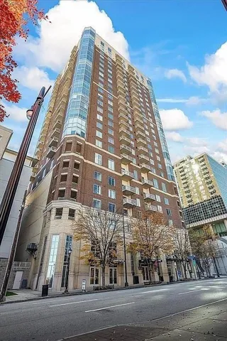 High-rise building featuring a brick facade with extensive window coverage, multiple balconies, and a distinctive curved glass corner