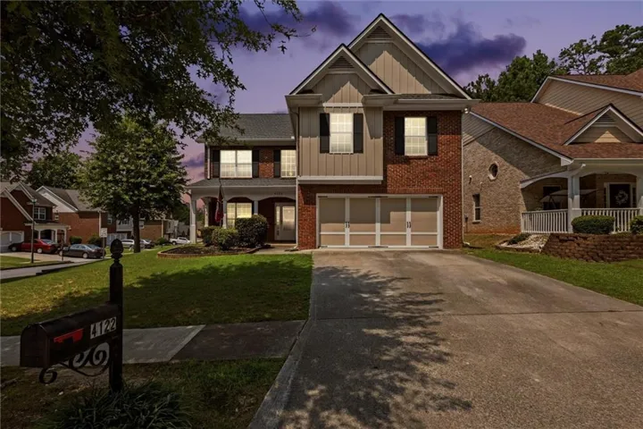 Two-story residence featuring a brick and siding exterior, an attached two-car garage with panel doors, a concrete driveway, and mature landscaping