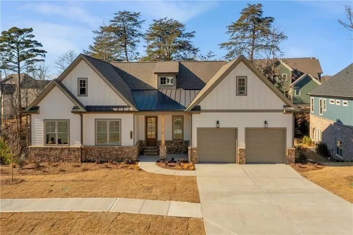 Contemporary farmhouse exterior featuring white board and batten and horizontal siding, a stone veneer foundation, a dark metal accent roof, and a two-car garage with carriage-style doors