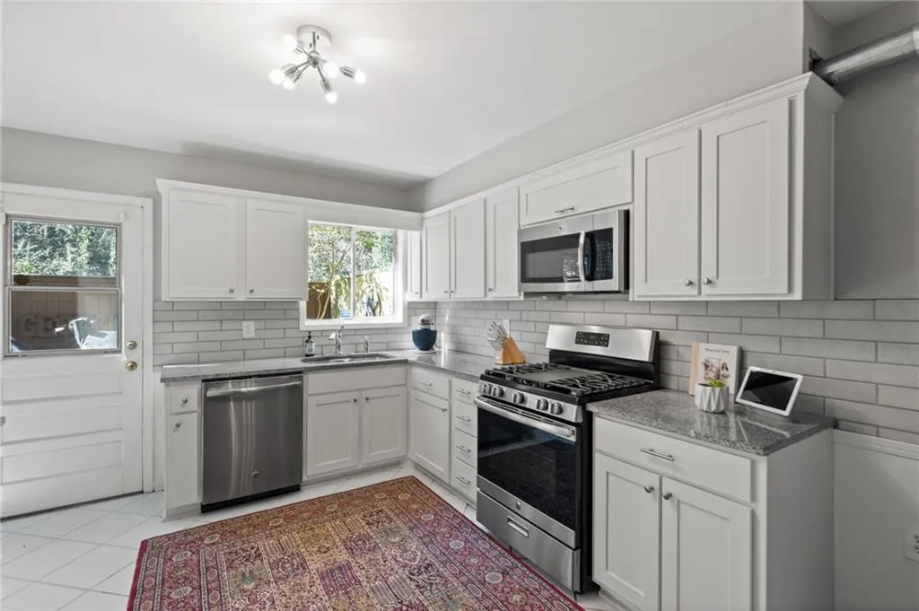 Kitchen featuring a notable chandelier, white cabinetry, sink, light tile floors, and stainless steel appliances