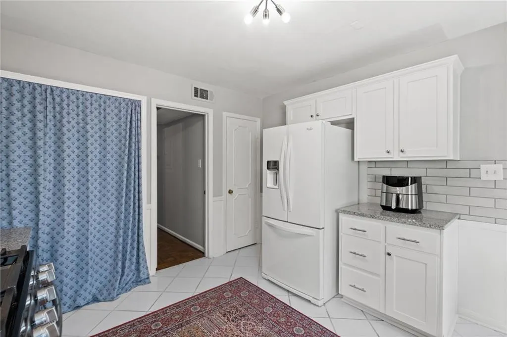 Kitchen featuring backsplash, white refrigerator with ice dispenser, white cabinets, light tile flooring, and stove
