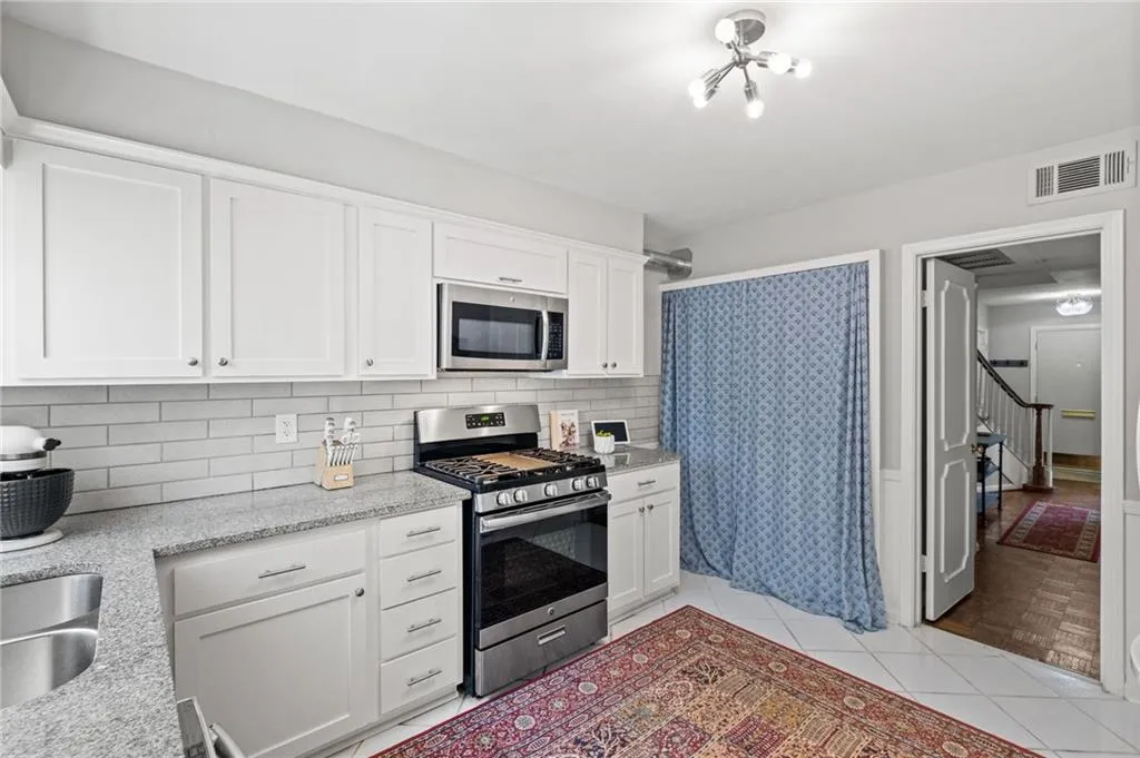 Kitchen with a notable chandelier, backsplash, stainless steel appliances, and white cabinets