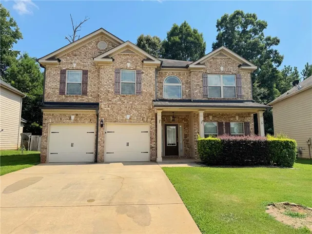 Two-story brick facade residence featuring a covered front porch with white columns, a two-car garage, and a concrete driveway