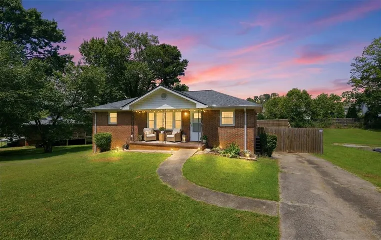 Brick exterior residence featuring a covered front porch, an arched entry walkway, a paved driveway, and established perimeter fencing