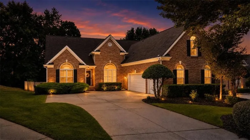 Brick exterior residence featuring arched windows with shutters, an attached garage, and a concrete driveway