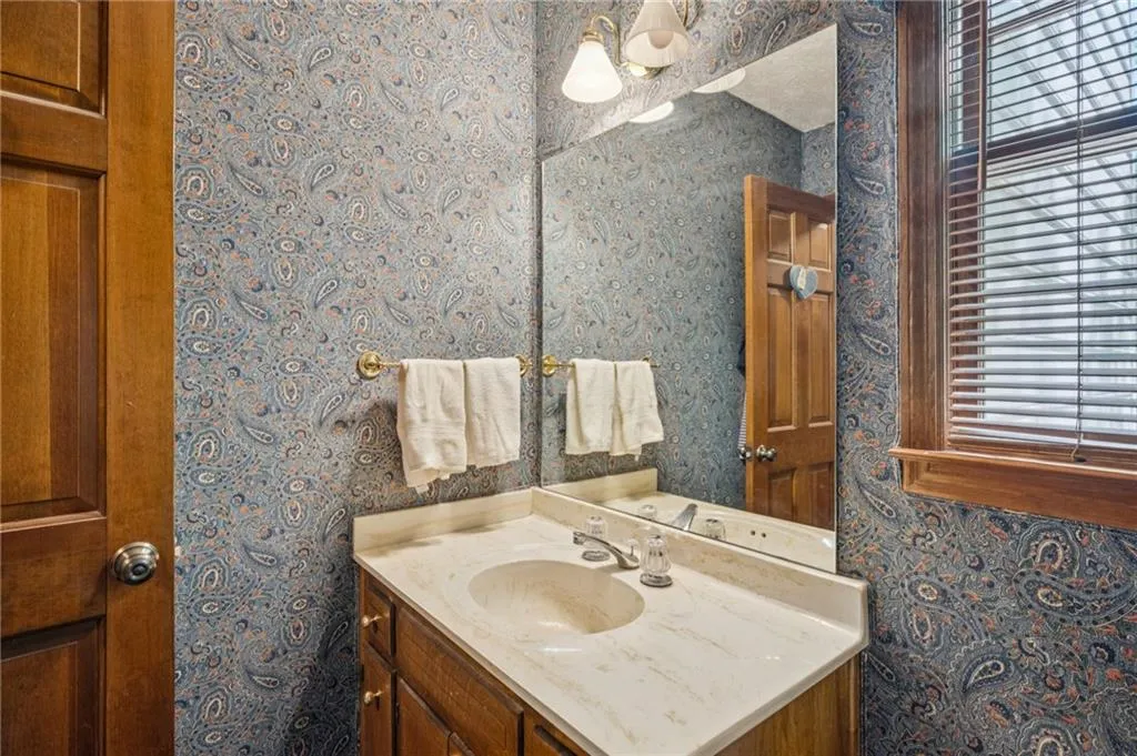 Half bath with wallpapered walls and vanity in between living room and kitchen.