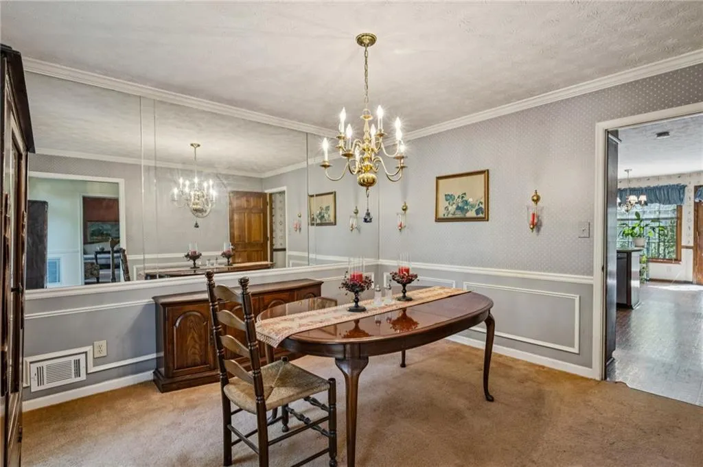 Formal dining room with chandelier, a wainscoted wall, wallpaper, a decorative wall, and a view to the kitchen.