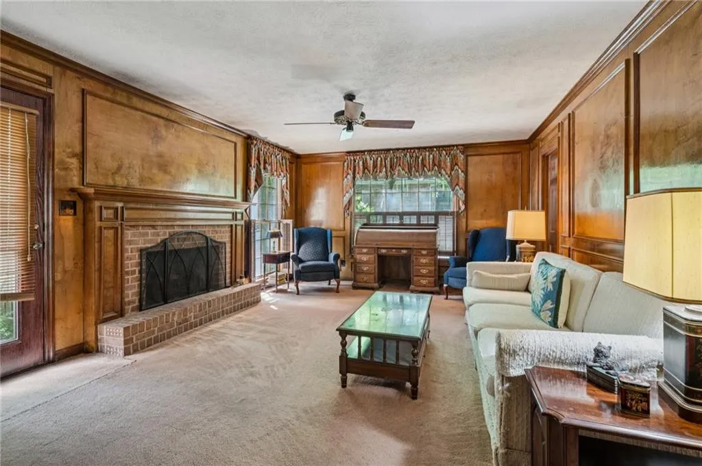 Living room featuring wood wall paneling, a brick fireplace, window treatments.