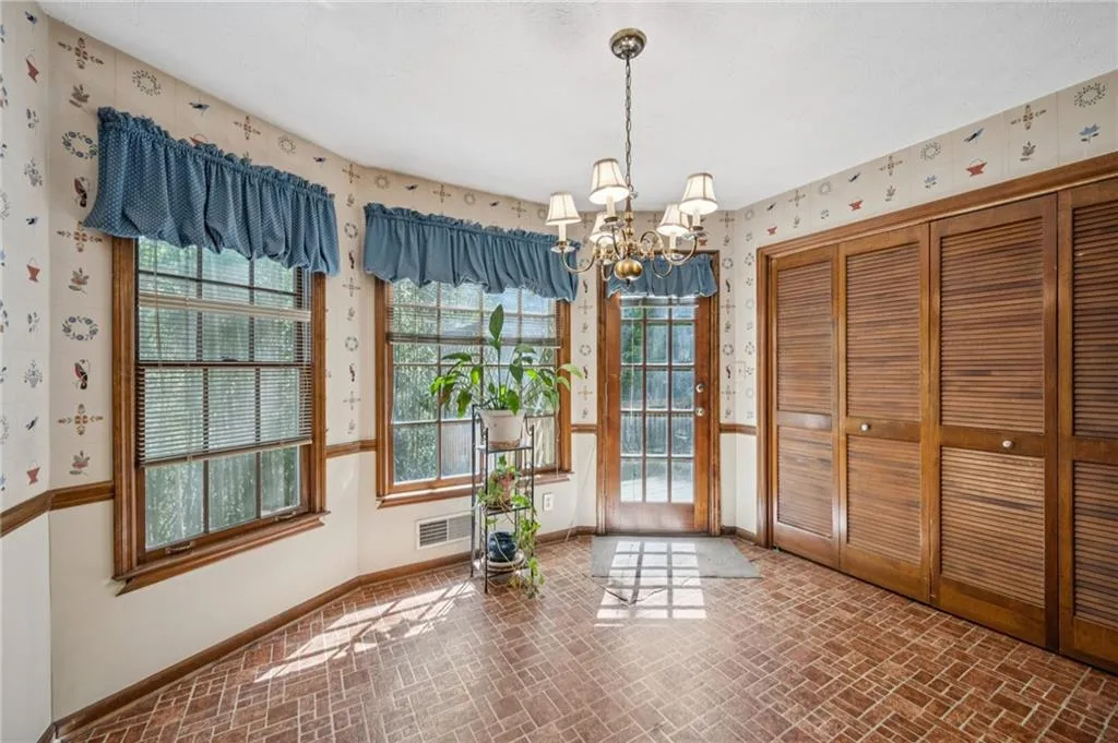 Unfurnished dining area featuring brick patterned flooring, hanging lights, wallpapered walls, and healthy amount of natural light