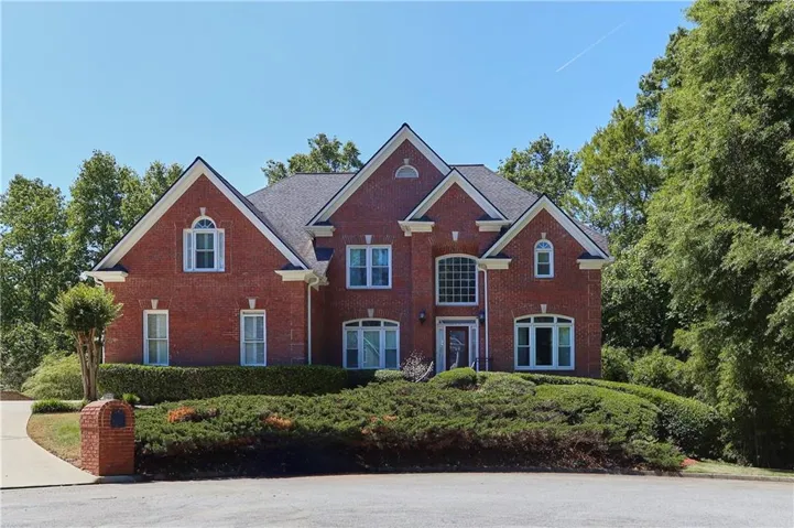 Red brick exterior with white trim, arched windows, and gabled rooflines, set on a landscaped lot with mature greenery