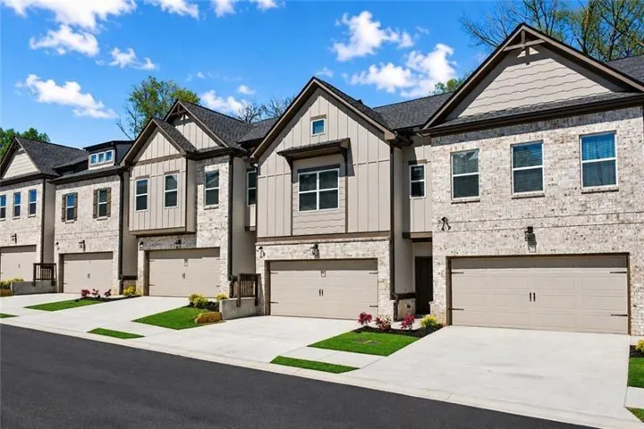 Contemporary townhome exterior featuring brick and vertical siding, pitched shingle roofs, integrated single-car garages, and concrete driveways