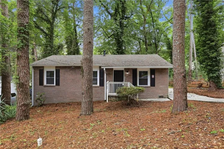 Brick exterior with dark shutters, front entry porch, and mature trees