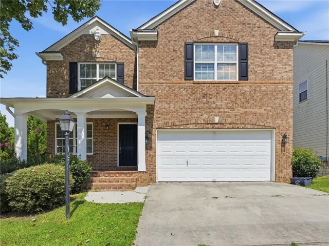 Brick exterior featuring a covered porch, white columns, and a two-car garage
