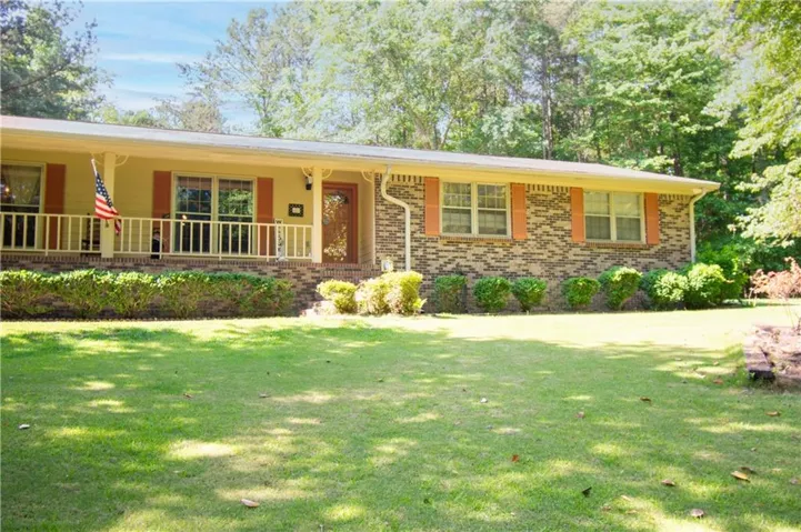 Traditional ranch-style residence featuring a brick facade, covered front porch, and a broad front lawn