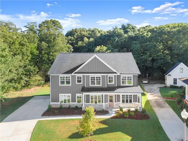 Two-story exterior with board and batten siding, stone accents, multiple large windows, a covered front porch, and an attached two-car garage