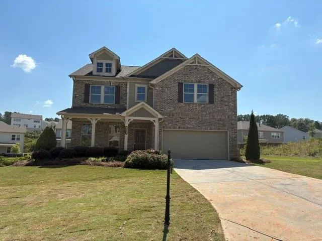 Two-story residence featuring a brick and siding exterior, covered front porch, dormer window, and an attached two-car garage