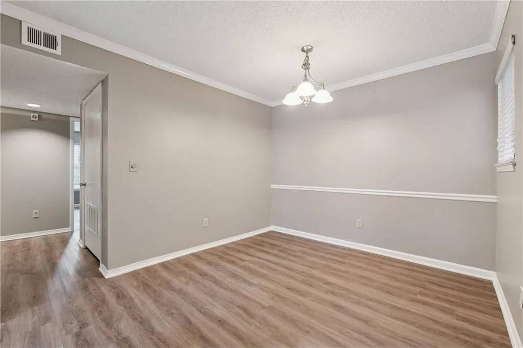 Spare room featuring a textured ceiling, crown molding, wood finished floors, and a chandelier