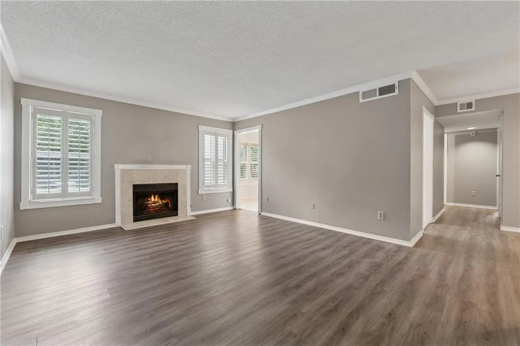 Unfurnished living room featuring crown molding, plenty of natural light, a high end fireplace, wood finished floors, and a textured ceiling