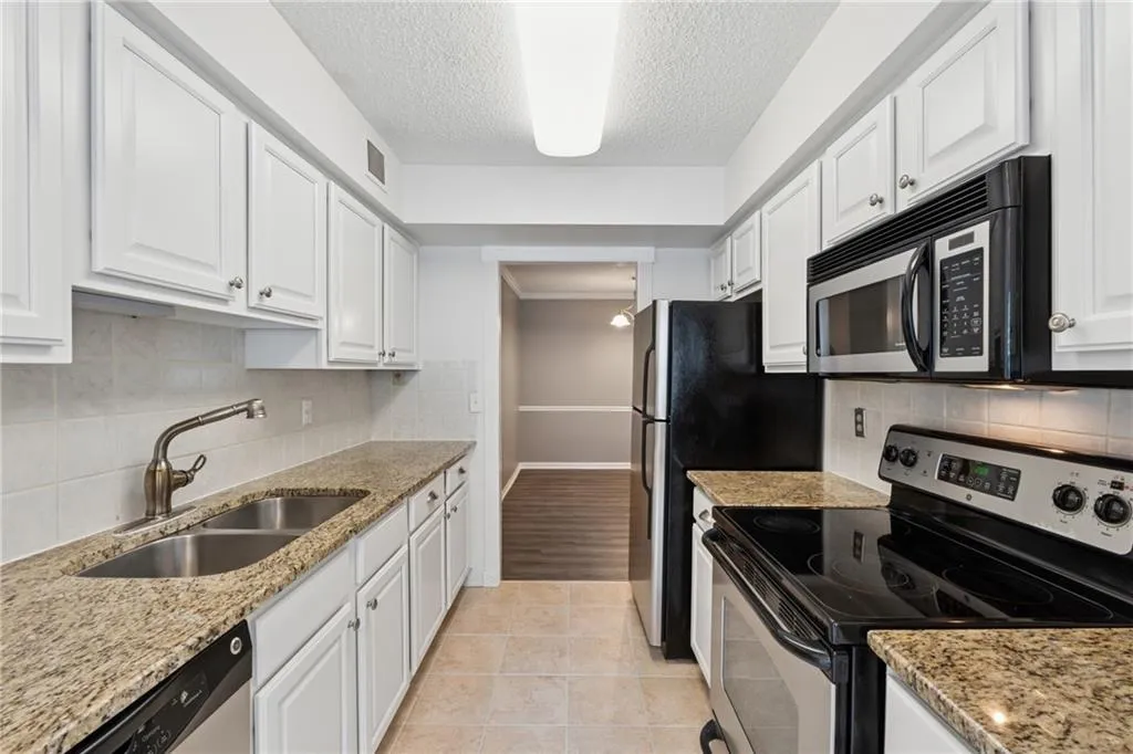 Kitchen with stainless steel appliances, decorative backsplash, light stone counters, white cabinets, and a textured ceiling