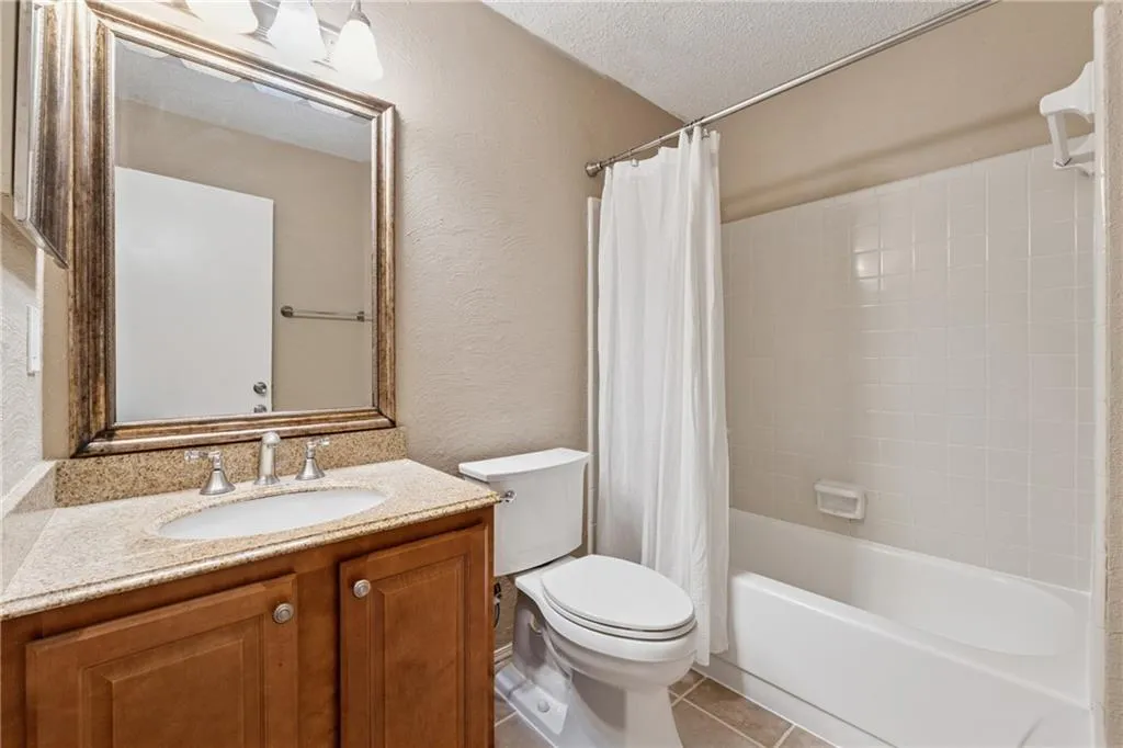 Full bath with a textured wall, light tile patterned flooring, shower / tub combo with curtain, vanity, and a textured ceiling