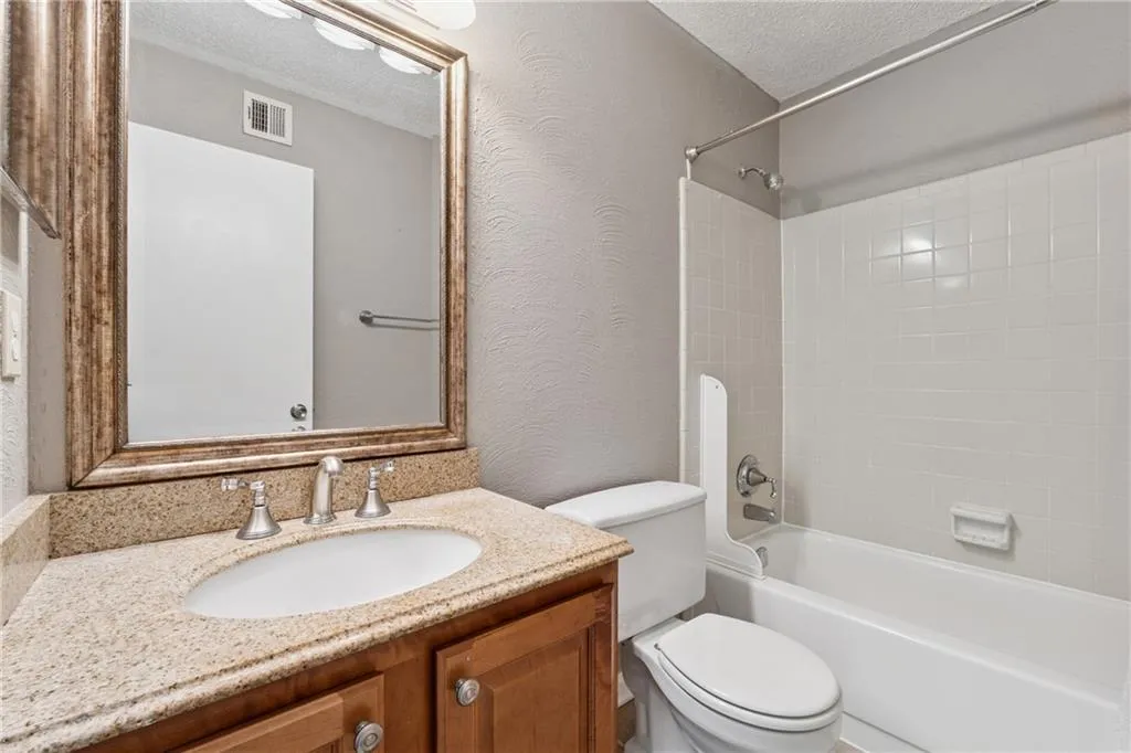 Bathroom with a textured wall, a textured ceiling, shower / bath combination, and vanity