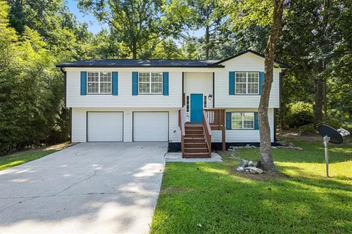Split-level residence featuring a white exterior, blue shutters, and a vibrant blue entry door