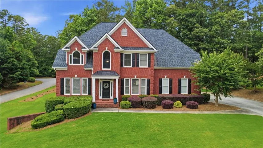 Traditional red brick exterior featuring a multi-gabled roofline, arched windows, manicured shrubs, and a paved driveway
