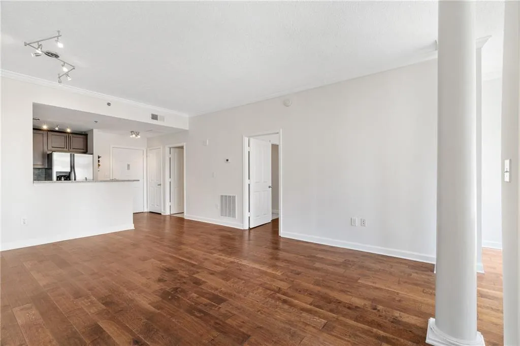 Unfurnished living room featuring dark wood finished floors, ornamental molding, ornate columns, and rail lighting