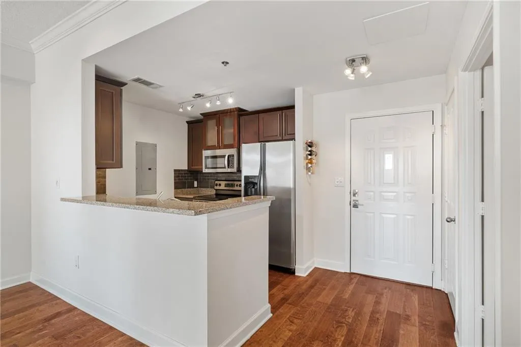 Kitchen featuring decorative backsplash, light stone countertops, stainless steel appliances, a peninsula, and dark wood-style floors