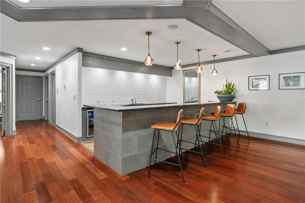 Indoor wet bar with dark countertops, dark wood finished floors, decorative light fixtures, beverage cooler, and recessed lighting