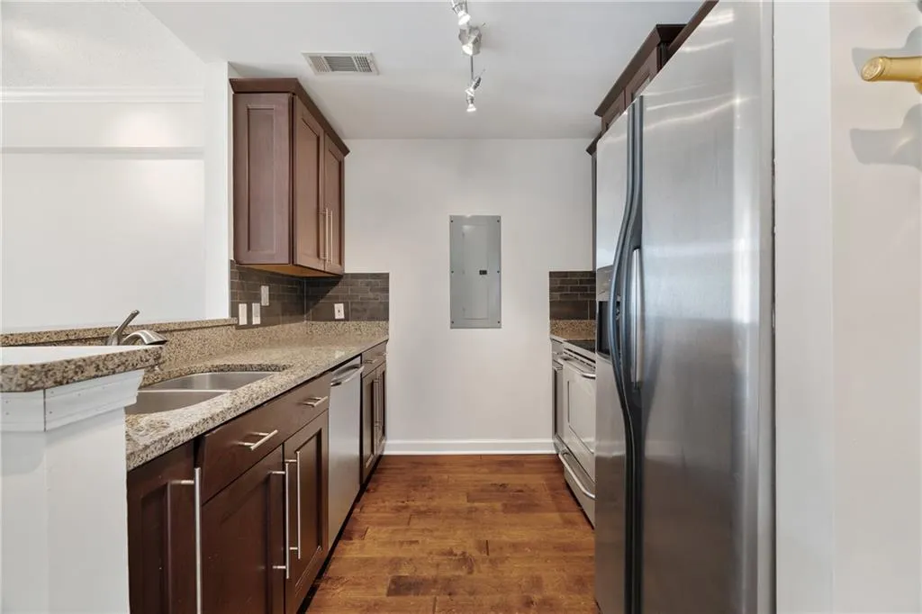 Kitchen with appliances with stainless steel finishes, light stone counters, dark wood-style flooring, tasteful backsplash, and electric panel