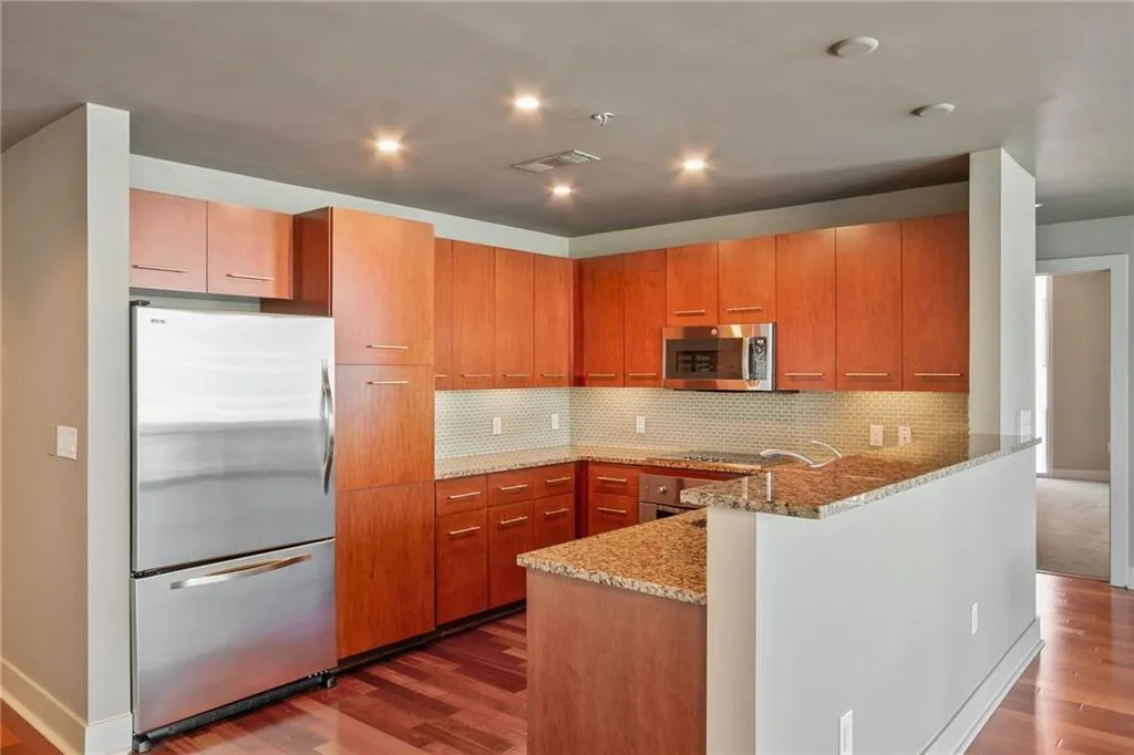 Kitchen featuring light stone countertops, appliances with stainless steel finishes, a peninsula, dark wood finished floors, and recessed lighting