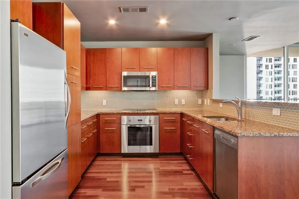 Kitchen with light stone countertops, stainless steel appliances, decorative backsplash, light wood-type flooring, and modern cabinets