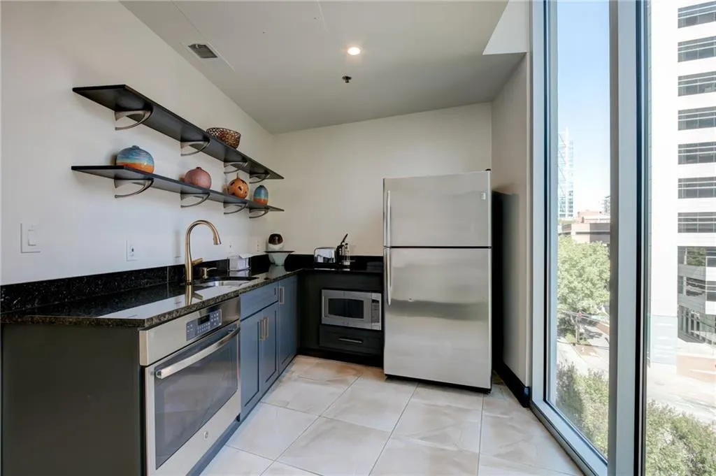 Club Room Kitchen featuring open shelves, stainless steel appliances, dark stone counters, and light tile patterned floors