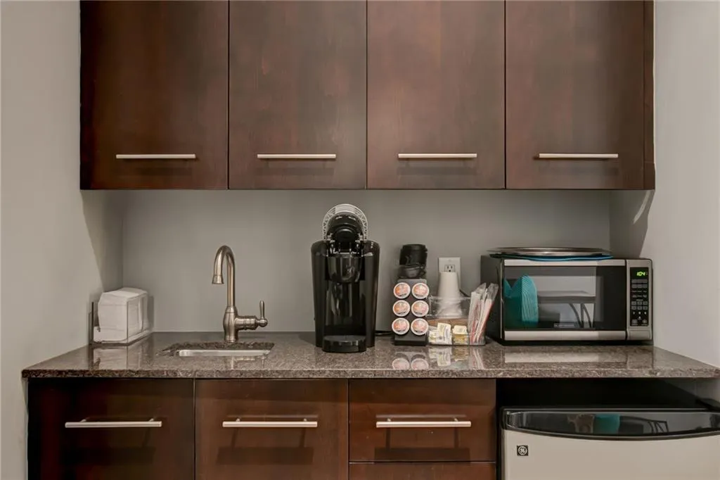 Guest Suite Bar featuring modern cabinets, stainless steel microwave, dark brown cabinetry, and dark stone counters