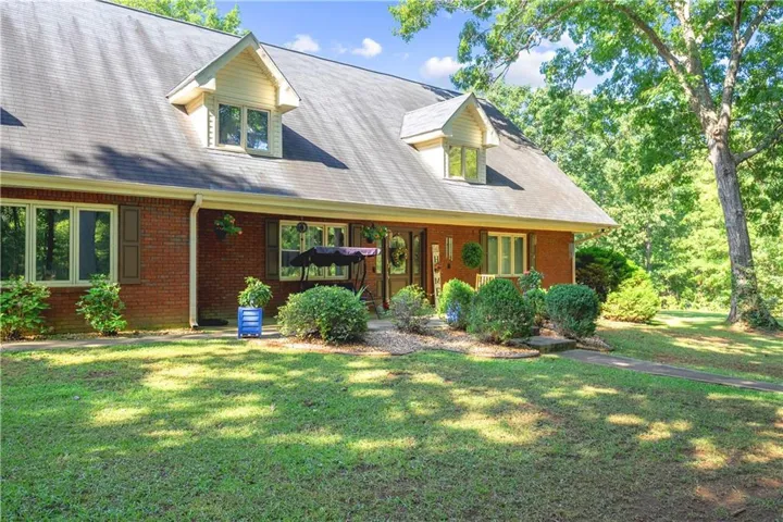Brick exterior with dormer windows, covered porch, and mature landscaping