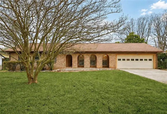 Brick exterior featuring arched windows, a single-car garage, and a concrete driveway