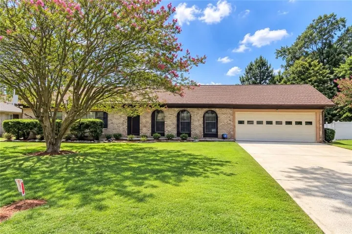 Brick exterior with arched windows, an attached two-car garage, mature landscaping, and an expansive concrete driveway