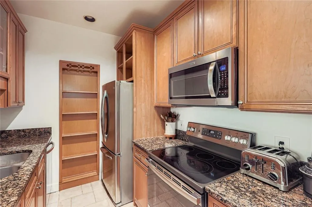 Kitchen with stainless steel appliances, open shelves, dark stone countertops, light tile patterned flooring, and brown cabinetry