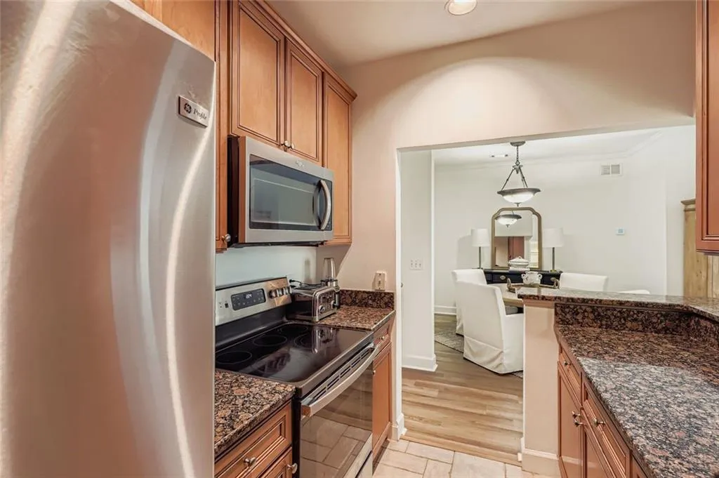 Kitchen featuring stainless steel appliances, dark stone countertops, decorative light fixtures, and brown cabinetry