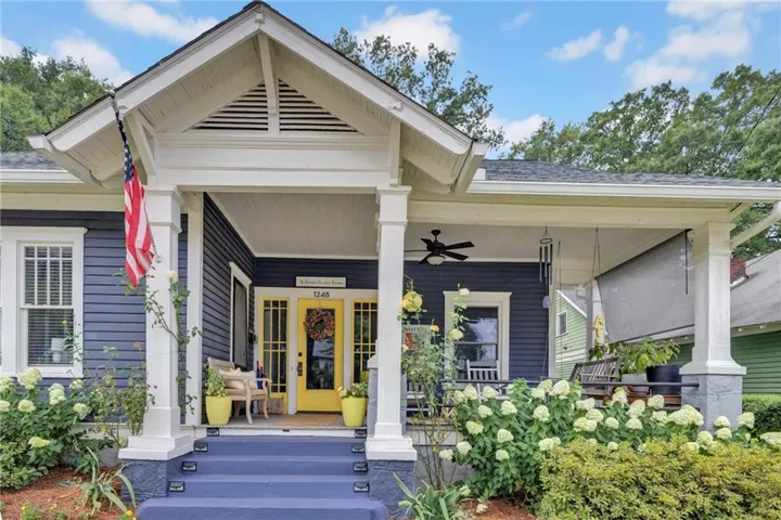 Craftsman-style home featuring a covered front porch with a ceiling fan, a vibrant yellow front door with sidelights, and mature front landscaping