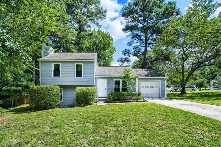 Split-level home featuring light blue siding, a covered entry, an attached garage, and a lush green lawn