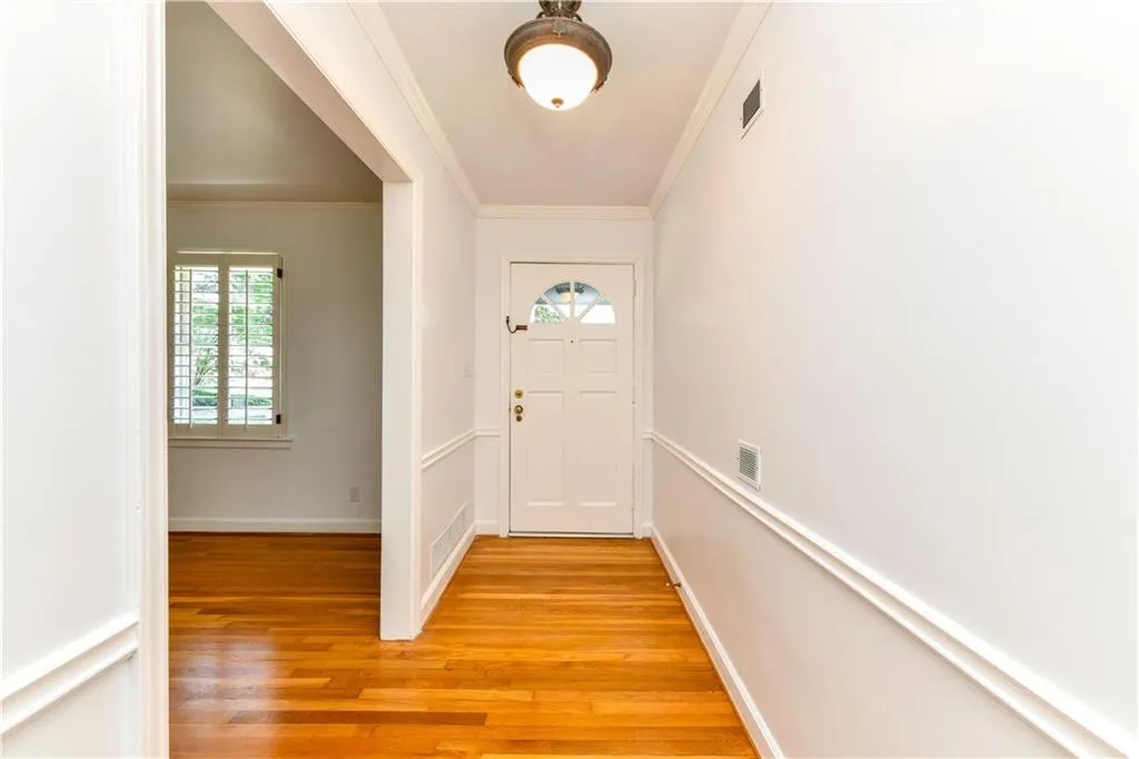 Doorway featuring light wood-style floors, visible vents, crown molding, and baseboards