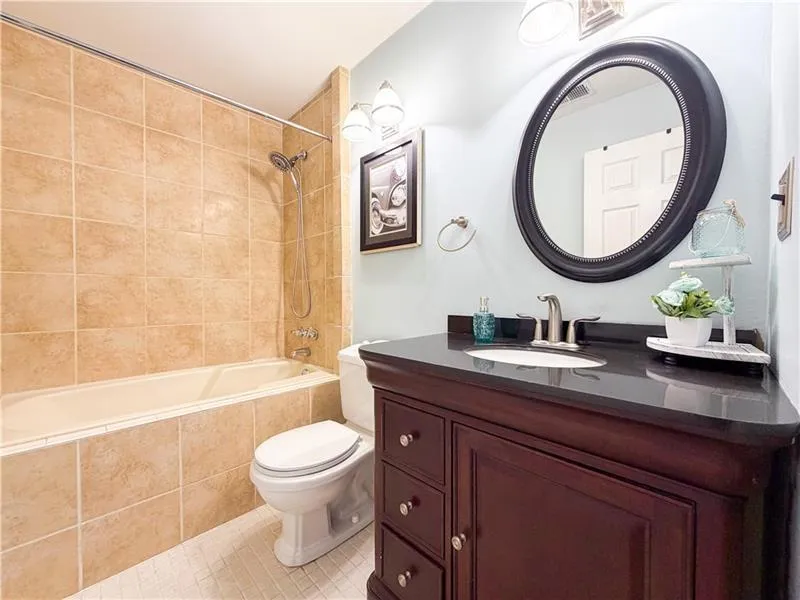 Built-in bathtub with shower system, tile surround, vanity with an integrated sink, and an oval mirror