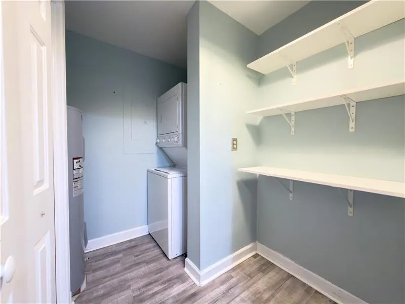 Utility area featuring wood-finish flooring, white shelving, and a stackable washer and dryer