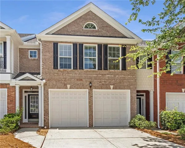 Brick facade townhome featuring a two-car garage, covered entry, black paneled door with glass inserts, upper-level windows with black shutters, and an arched transom window