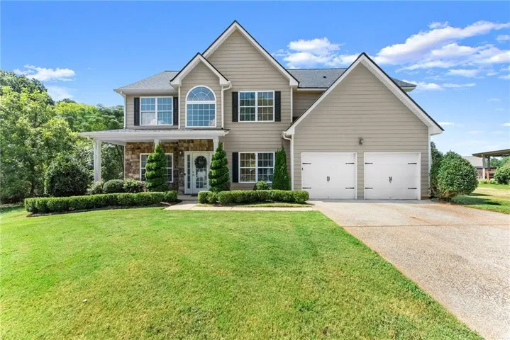 Two-story exterior with light-toned siding, a stone facade, a covered front porch, and a two-car garage