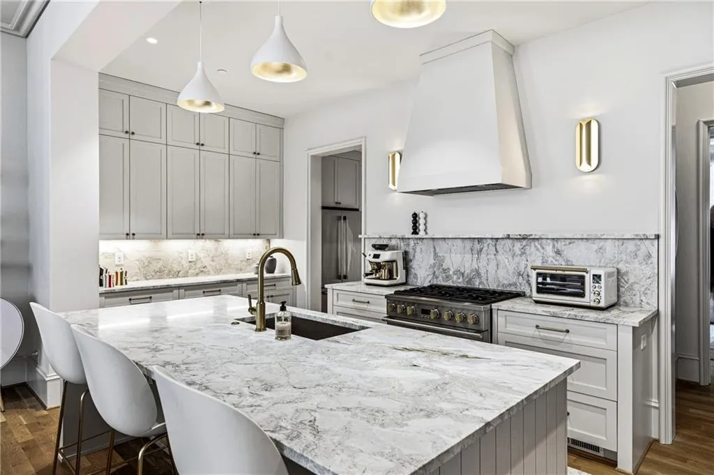 Gourmet kitchen featuring a substantial island with integrated sink, panel cabinetry, range with custom hood, and natural stone countertops and backsplash