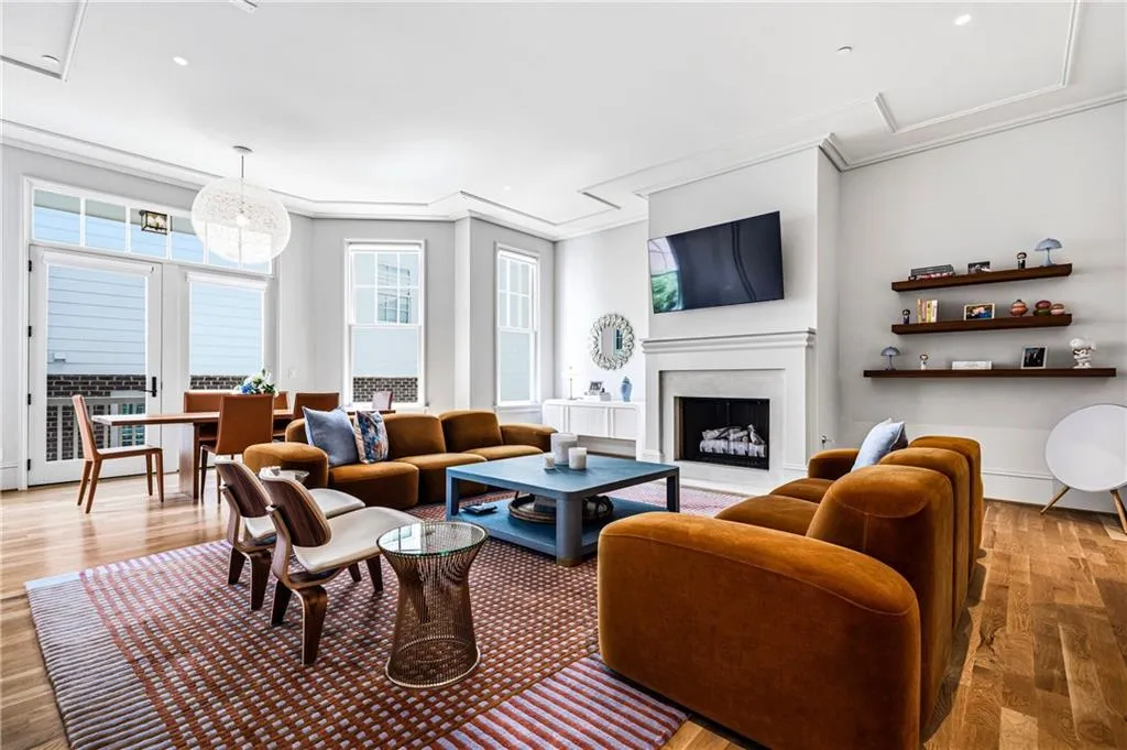 Spacious living area featuring light wood-finish flooring, a white mantel fireplace, and built-in floating shelves