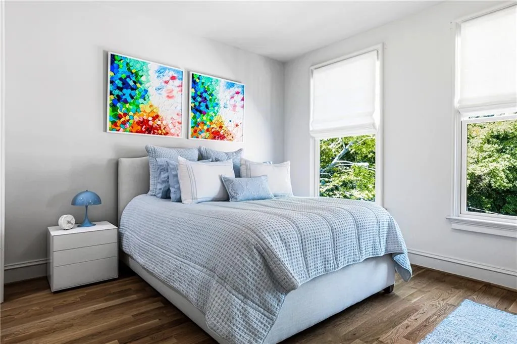 Spacious room featuring wood-finish flooring, white walls, and two large windows with white shades